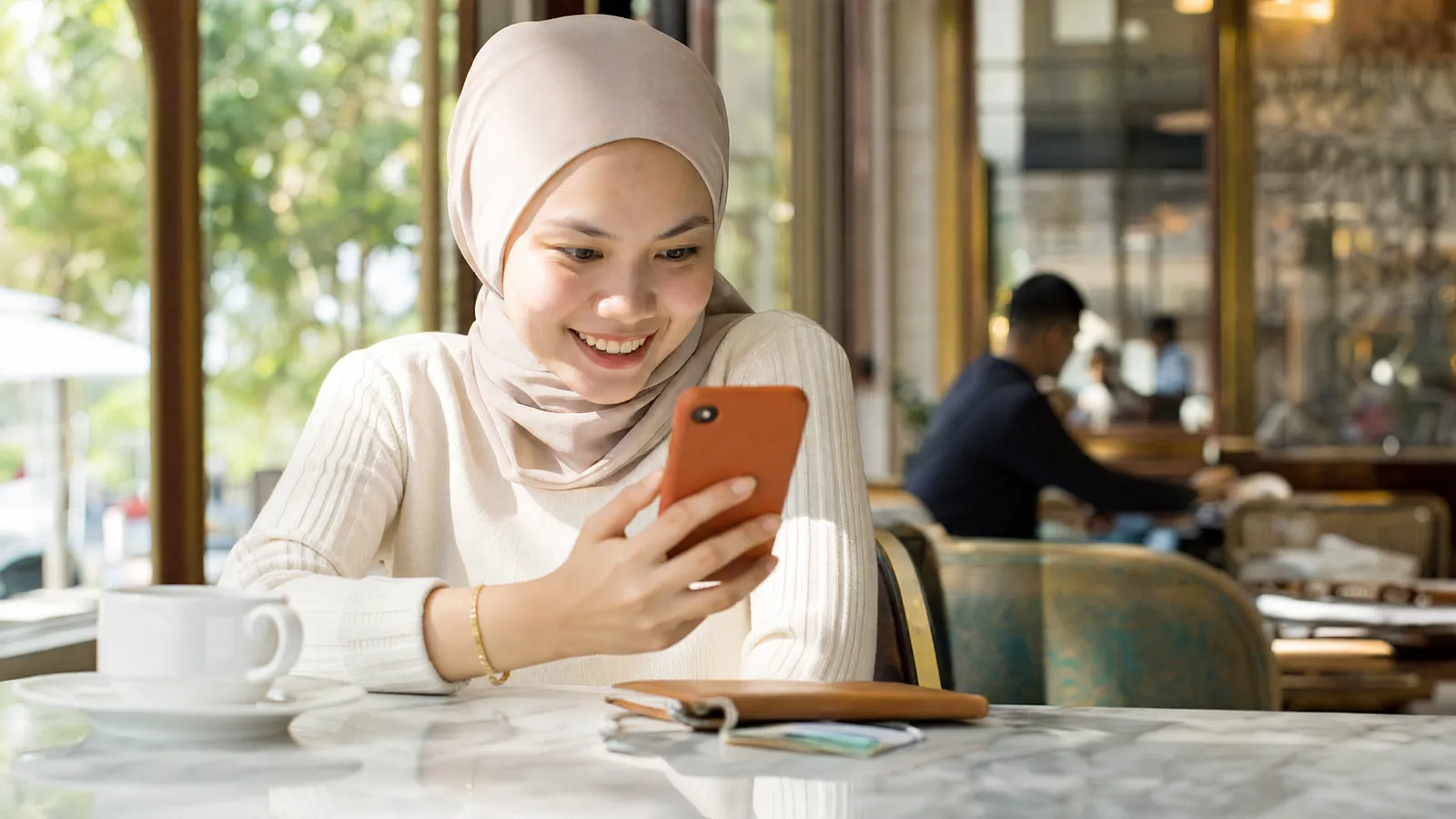 A creator smiling at good news on her phone at a sunlit café table